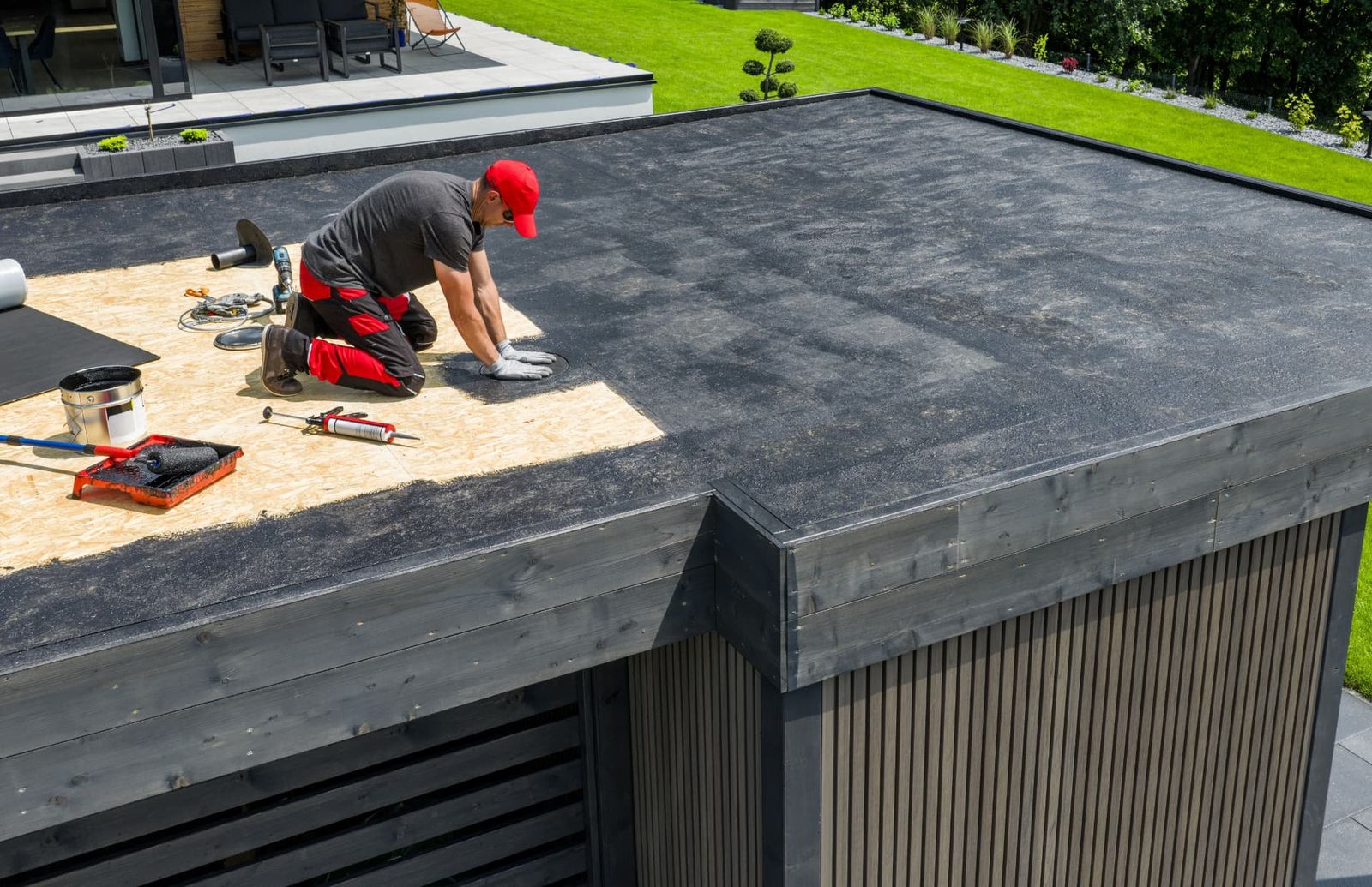A roofer laying black membrane over the exposed decking of a flat roof.
