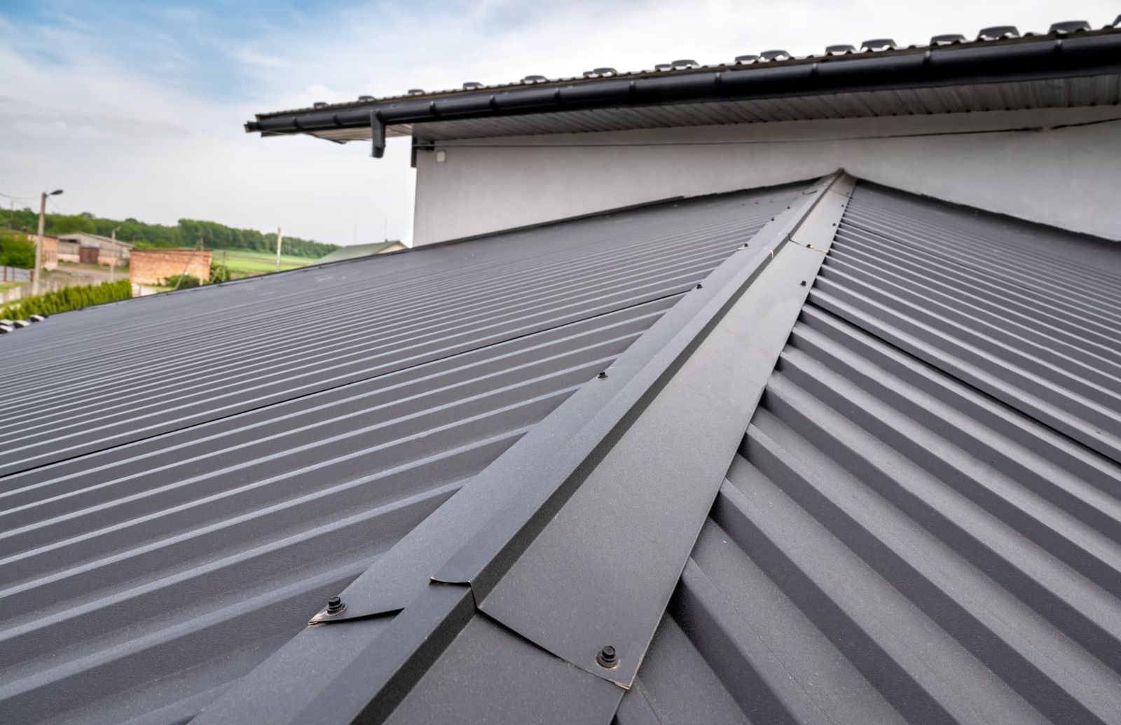 Dark grey standing seam metal panels running up to a hip, with a black gutter along the eave.