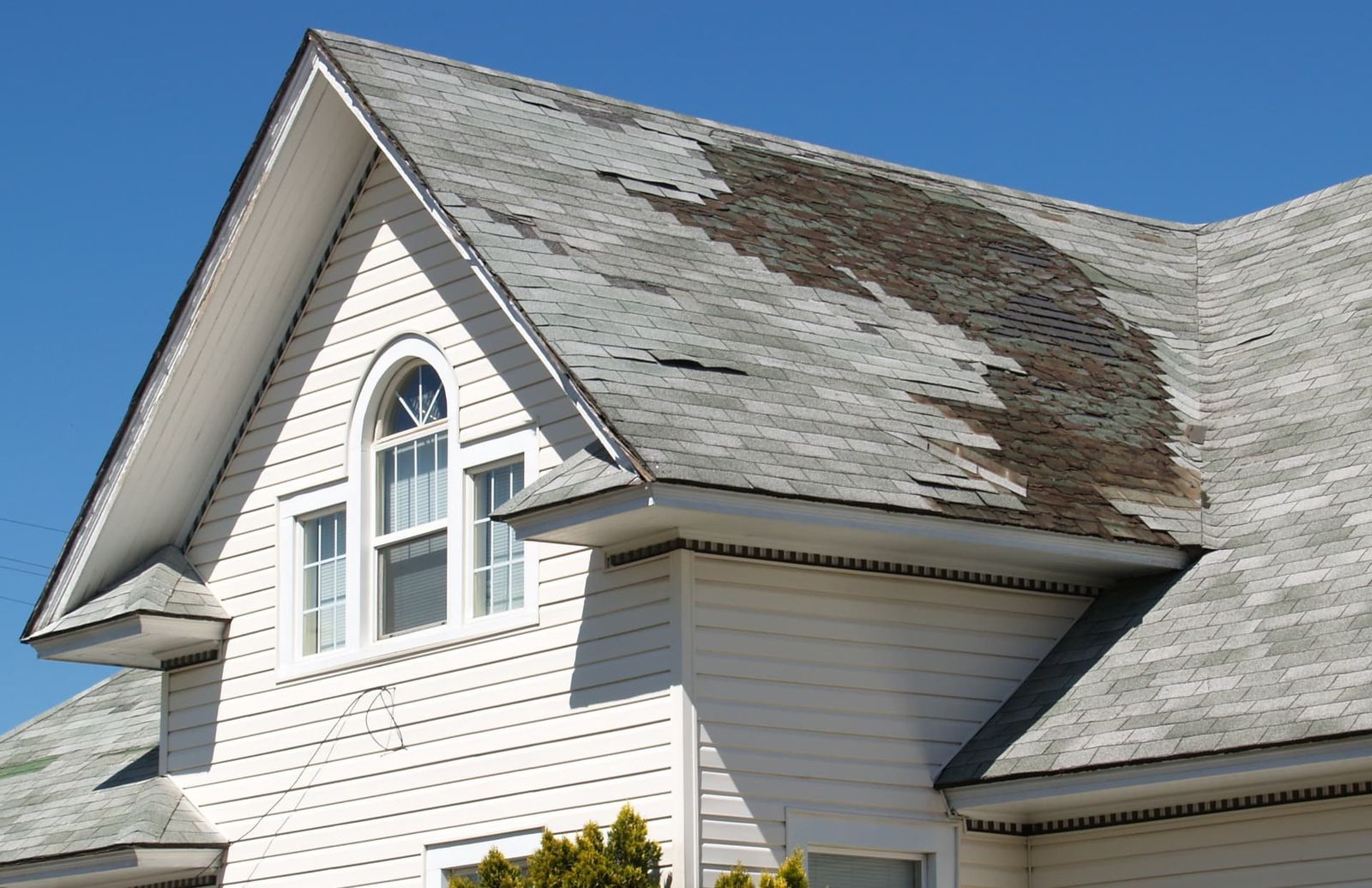 A shingle roof slope with patches of shingles missing, exposing the layer underneath.